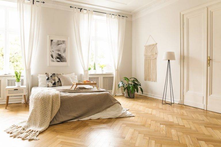 Blanket on bed with wooden tray in spacious bright bedroom interior with wood flooring